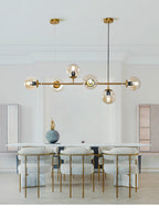 In a pale room with arched cabinetry and cream chairs, this Clérachic pendant hangs six amber orbs along a brass rod.