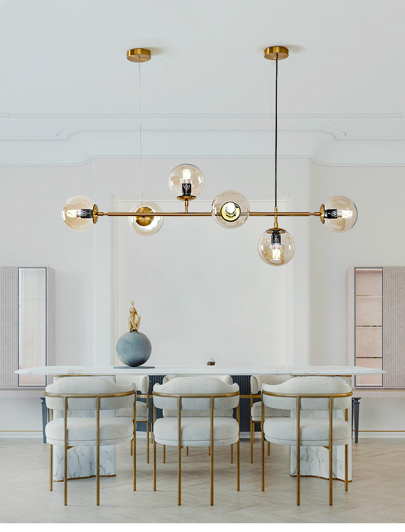 In a pale room with arched cabinetry and cream chairs, this Clérachic pendant hangs six amber orbs along a brass rod.