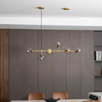 Lit amber glass orbs along a brass rod, over a dark wood panelled wall and a marble table, in this Clérachic pendant.