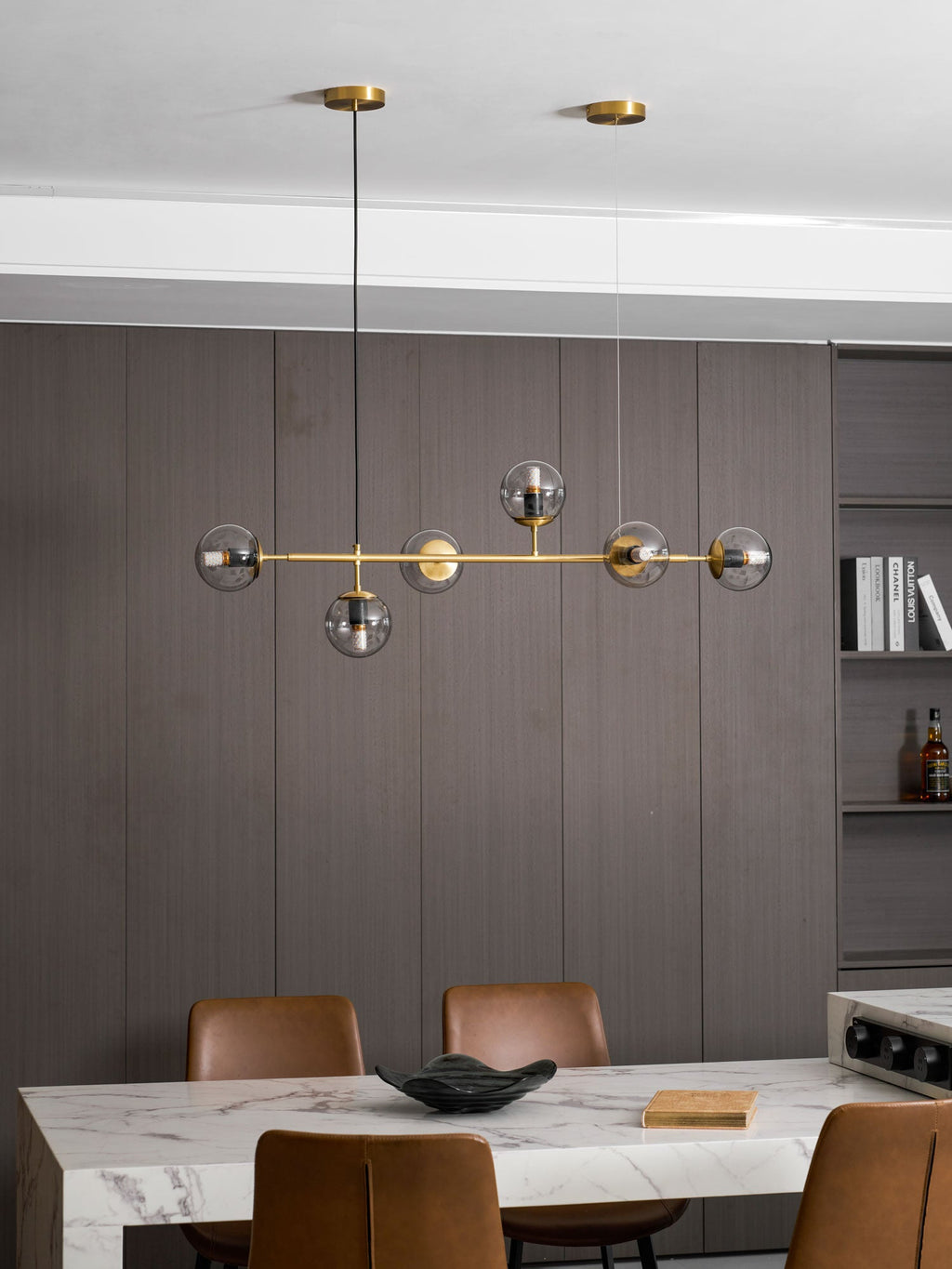 A wider view of this Clérachic pendant hanging in front of grey-brown panelling, above a marble counter with tan leather chairs.