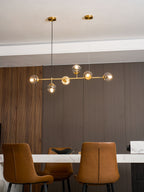With a walnut panel at the left, this Clérachic pendant's lit orbs line up on a brass rod above a marble-topped table.