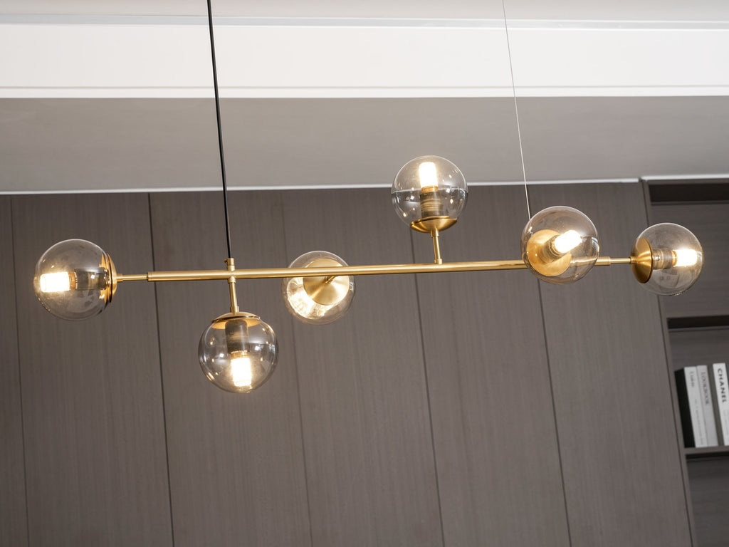 Close view of the lit amber glass orbs and slim brass rod of this Clérachic pendant against a dark panelled wall.