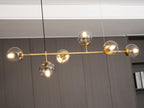 Close view of the lit amber glass orbs and slim brass rod of this Clérachic pendant against a dark panelled wall.