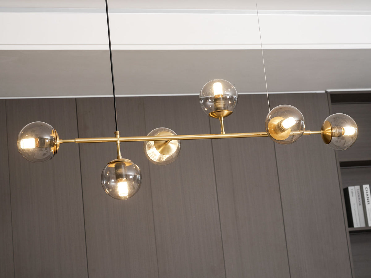 Close view of the lit amber glass orbs and slim brass rod of this Clérachic pendant against a dark panelled wall.