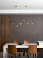 High in a panelled dining room, the brass rod and smoky orbs of this Clérachic pendant hang above a marble table and leather chairs.