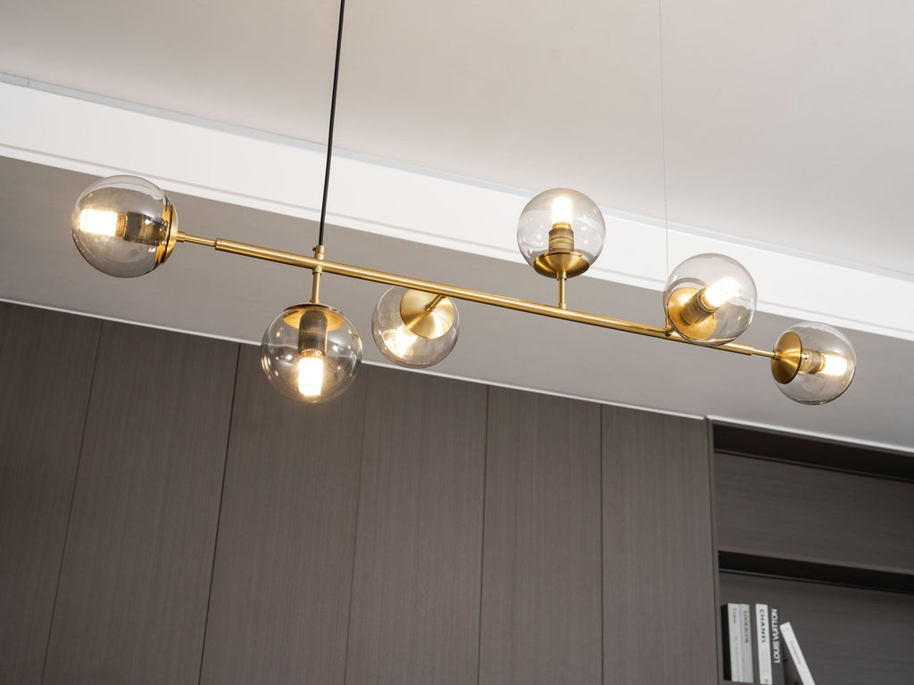 Angled view from below of this Clérachic pendant, with lit clear orbs on a brass rod beside a white ceiling edge and dark wall.