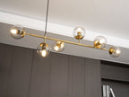 Angled view from below of this Clérachic pendant, with lit clear orbs on a brass rod beside a white ceiling edge and dark wall.