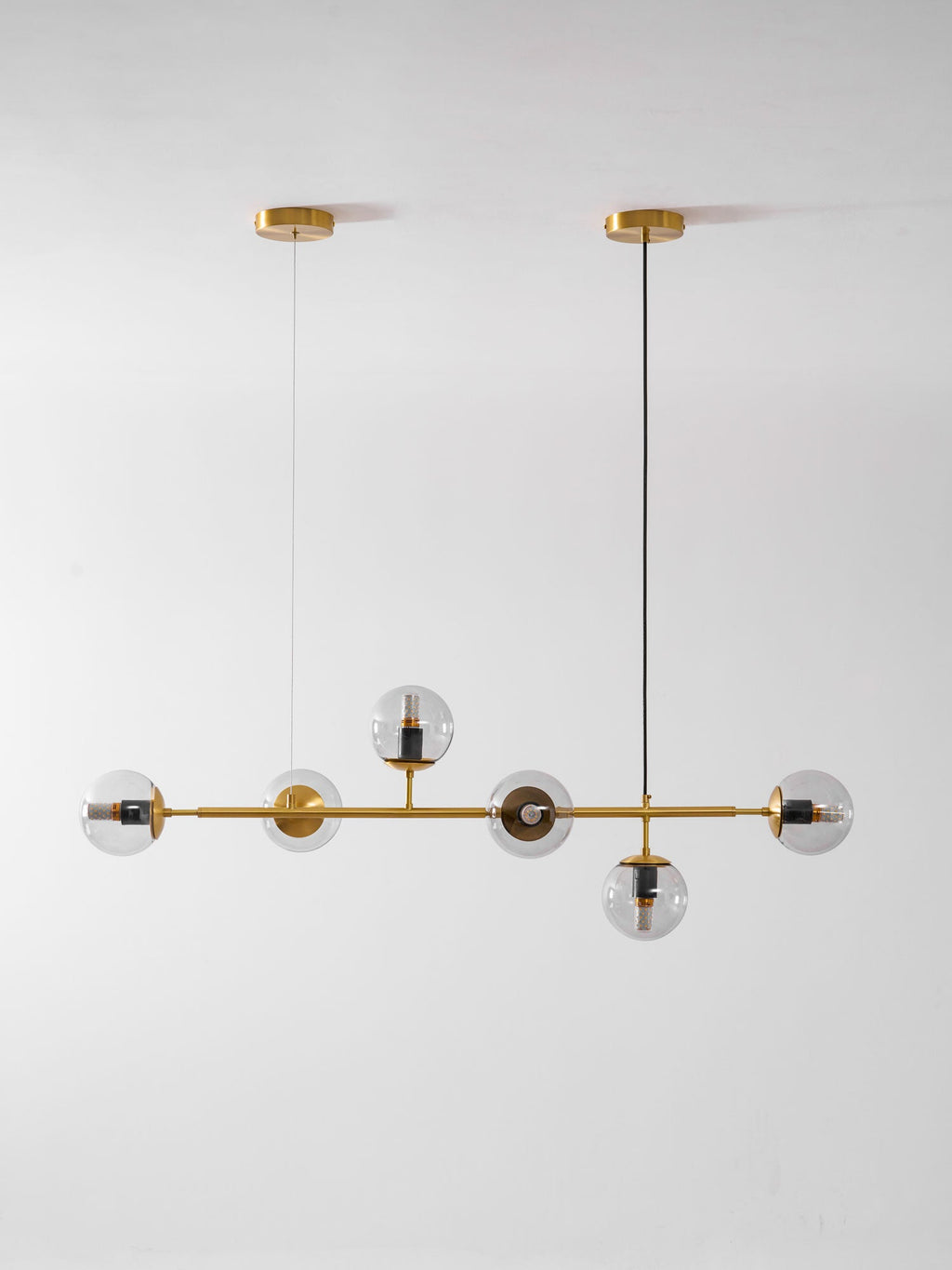 A tall studio view of this Clérachic pendant on light grey, with clear orbs along a brass rod and two ceiling canopies.