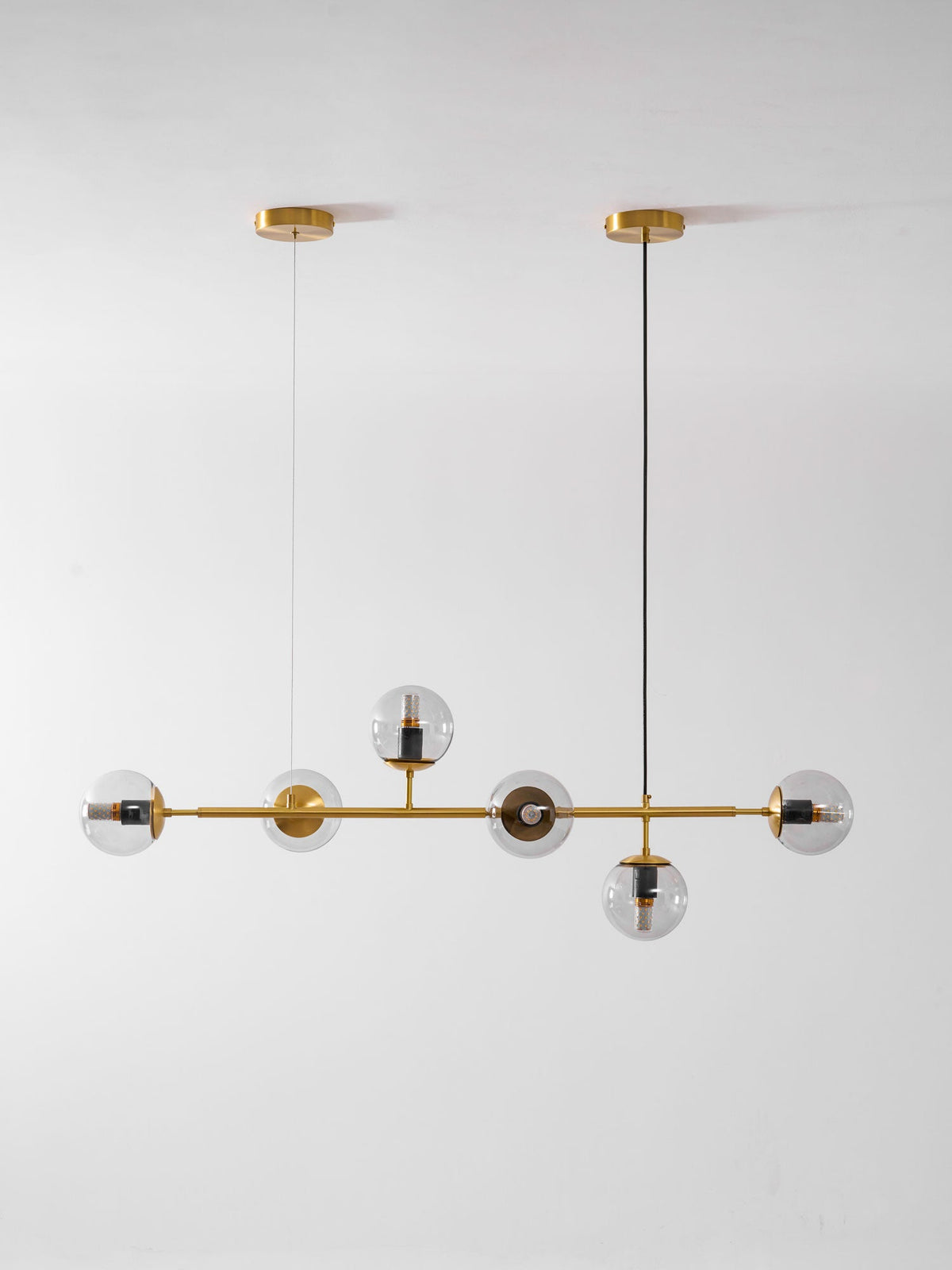 A tall studio view of this Clérachic pendant on light grey, with clear orbs along a brass rod and two ceiling canopies.
