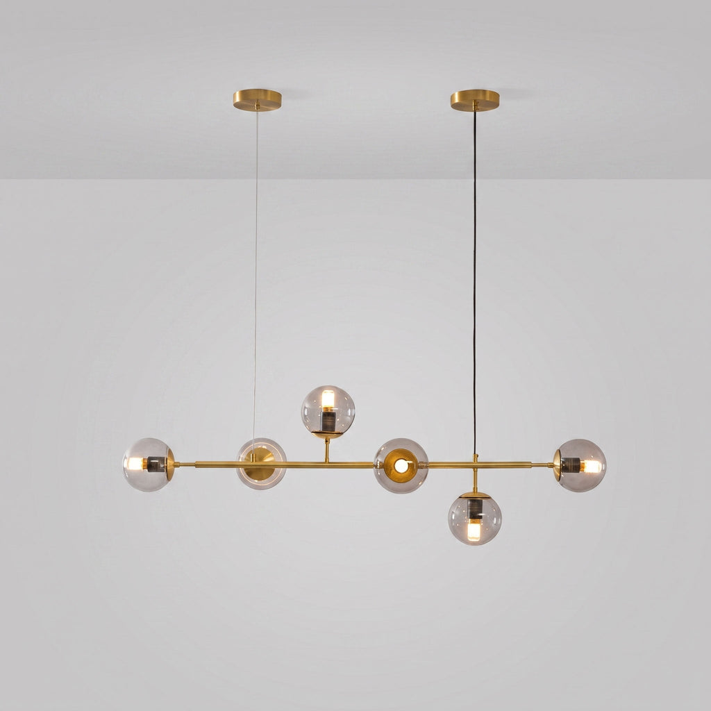 Clear glass orbs lit warm along a brass rod, on a light grey studio backdrop, in this Clérachic pendant with brass canopies.