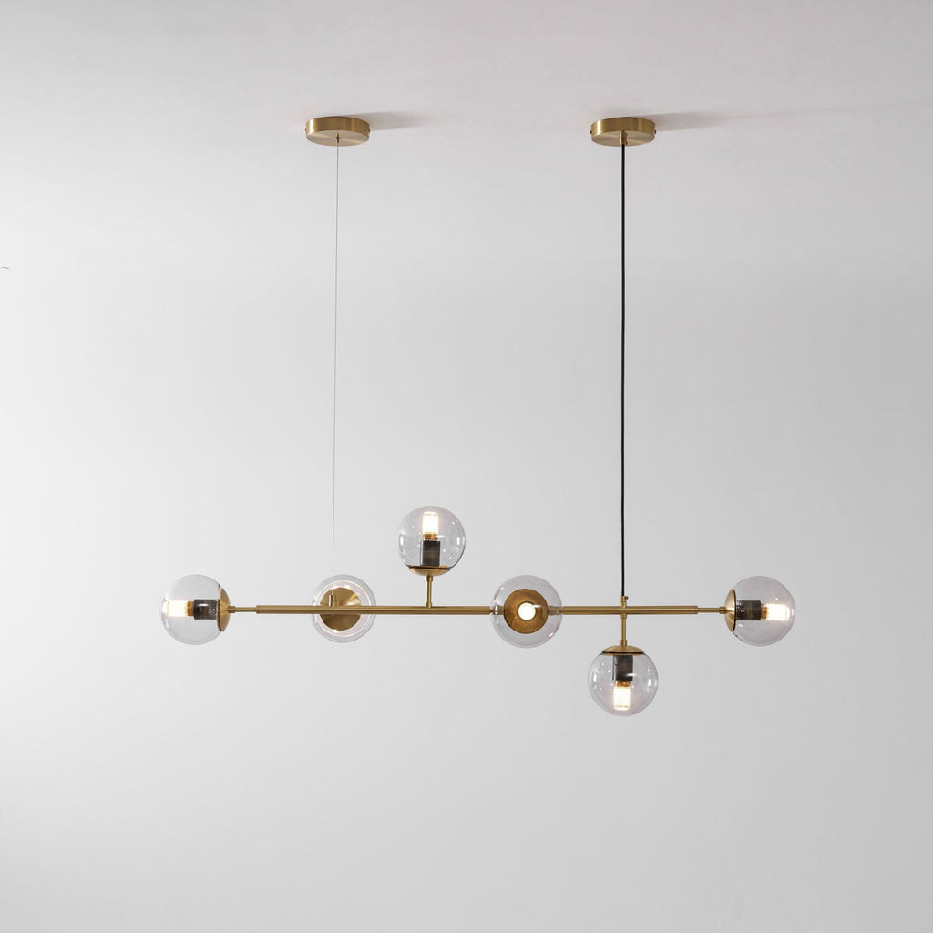 Straight-on studio view of this Clérachic pendant, with its brass rod, two canopies and six lit clear orbs on pale grey.