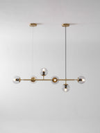 A smaller studio view of this Clérachic pendant on pale grey, six clear orbs lit along a brass rod from two brass canopies.