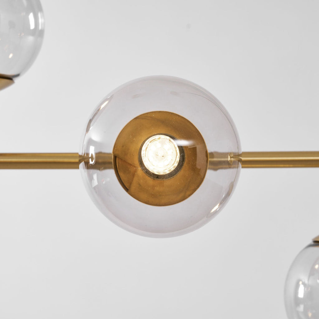 Close view of one clear glass orb on this Clérachic pendant, lit, with a brass-lined holder and the brass rod at either side.