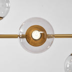 Close view of one clear glass orb on this Clérachic pendant, lit, with a brass-lined holder and the brass rod at either side.
