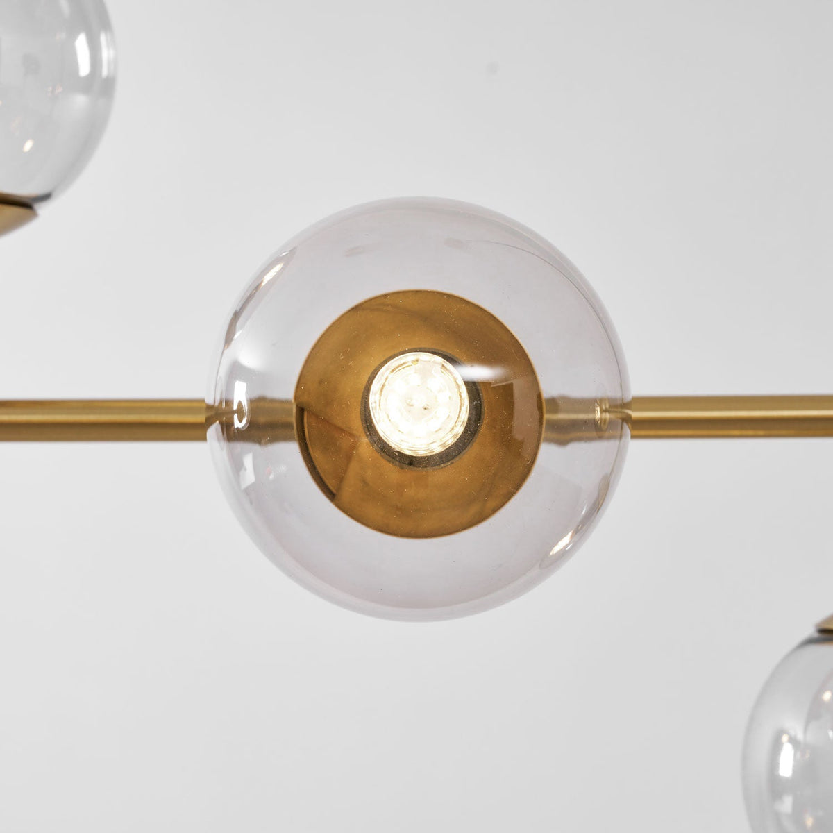 Close view of one clear glass orb on this Clérachic pendant, lit, with a brass-lined holder and the brass rod at either side.