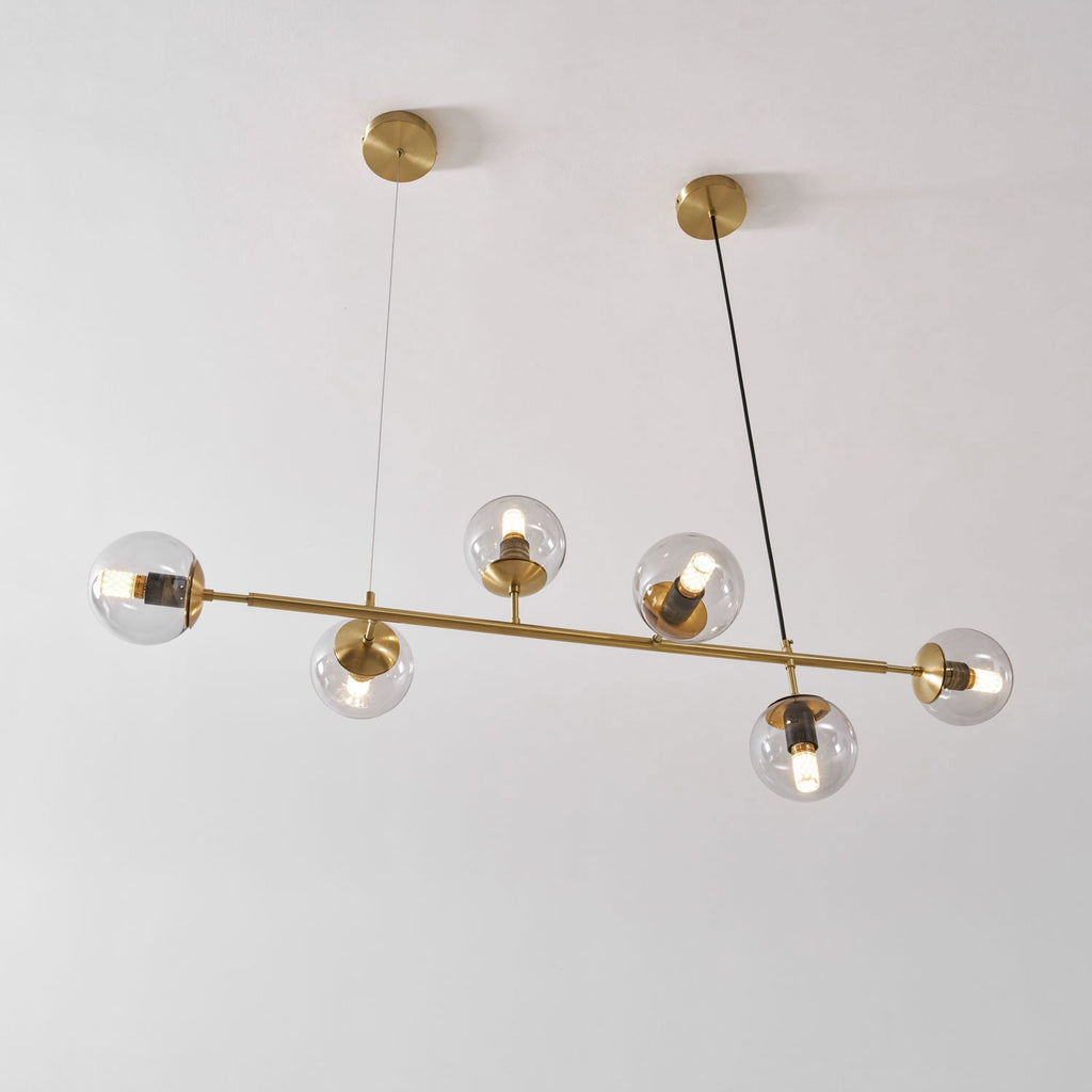 Seen at a slight angle against a white wall, this Clérachic pendant's lit clear orbs sit on a brass rod and two canopies.