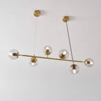 Seen at a slight angle against a white wall, this Clérachic pendant's lit clear orbs sit on a brass rod and two canopies.