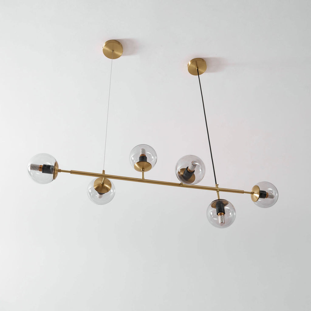 The same brass rod and clear orbs of this Clérachic pendant, switched off, angled from below against a pale wall.