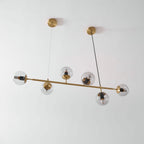 The same brass rod and clear orbs of this Clérachic pendant, switched off, angled from below against a pale wall.