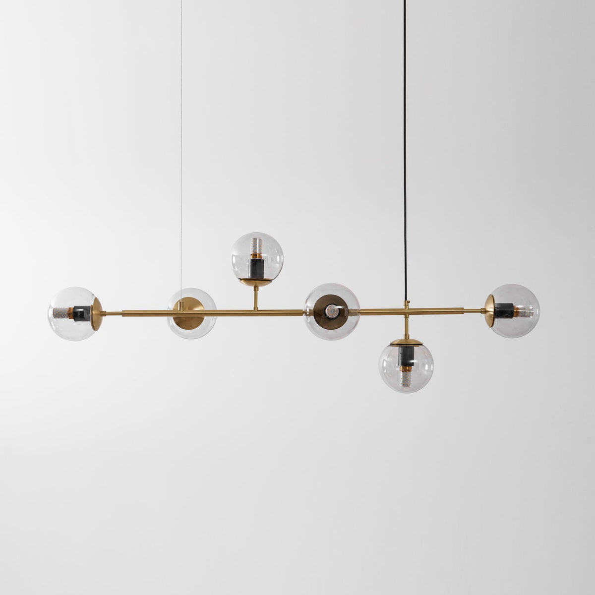 A straight-on view of this Clérachic pendant, its clear orbs unlit, with a black cord rising to a ceiling point at the right.