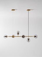 Smaller in frame, this Clérachic pendant hangs from two brass canopies, with six clear orbs on a brass rod on a pale wall.