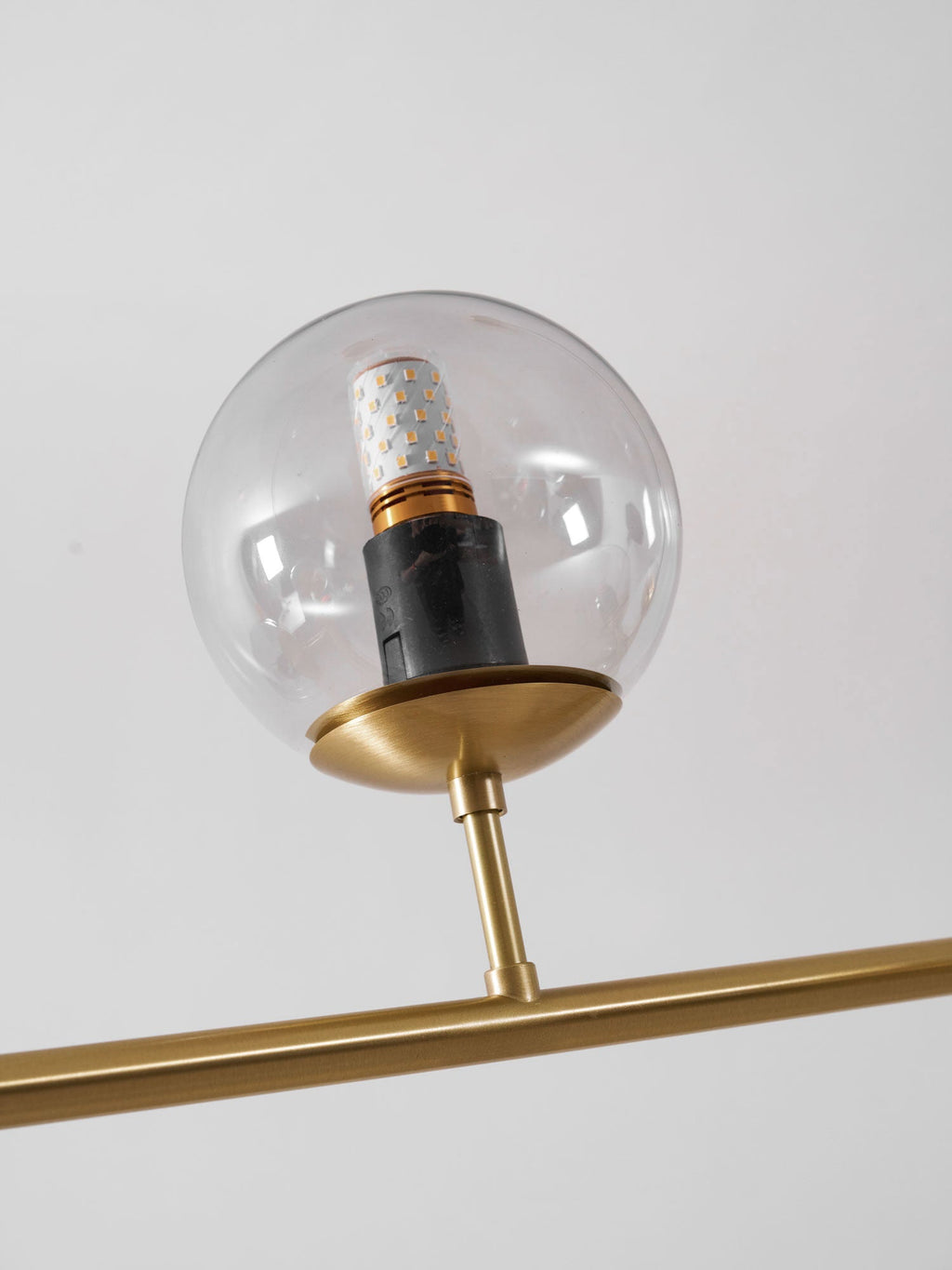 Close view of a single clear glass orb on this Clérachic pendant, with a black bulb holder and a brass cup on the rod.