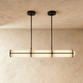 Clérachic long opal tube pendant with black metal bands, hung from two slim rods against a limewash wall and plaster ceiling.