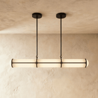 Clérachic long opal tube pendant with black metal bands, hung from two slim rods against a limewash wall and plaster ceiling.