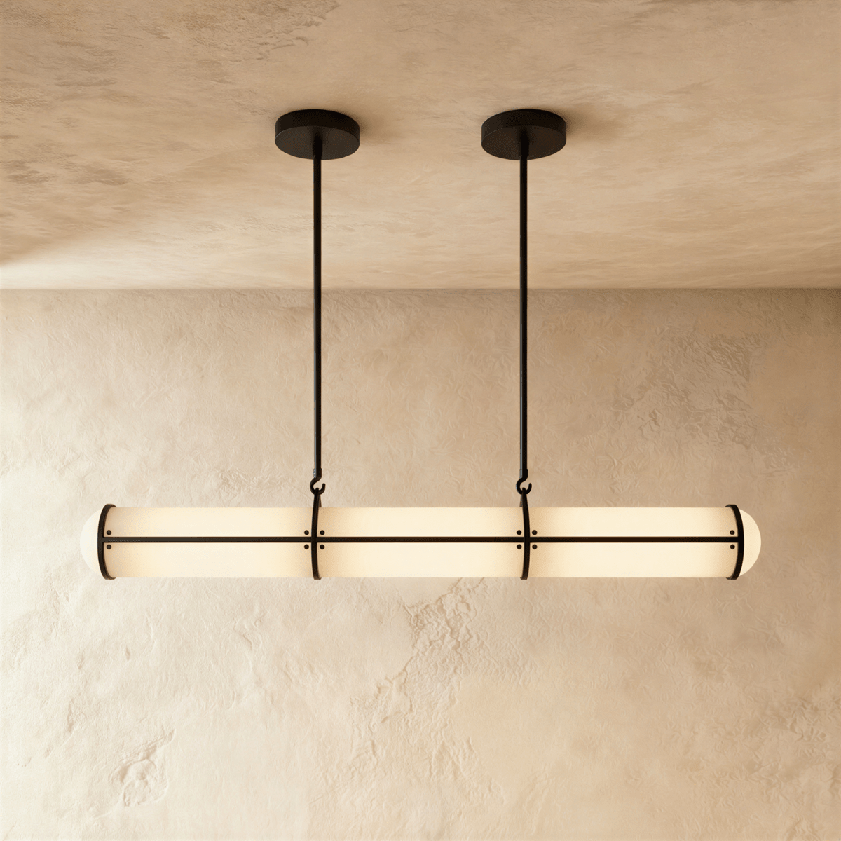 Clérachic long opal tube pendant with black metal bands, hung from two slim rods against a limewash wall and plaster ceiling.