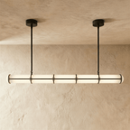 Clérachic extra-long opal tube pendant with black bands and two slim hanging rods, glowing softly in front of a textured wall.