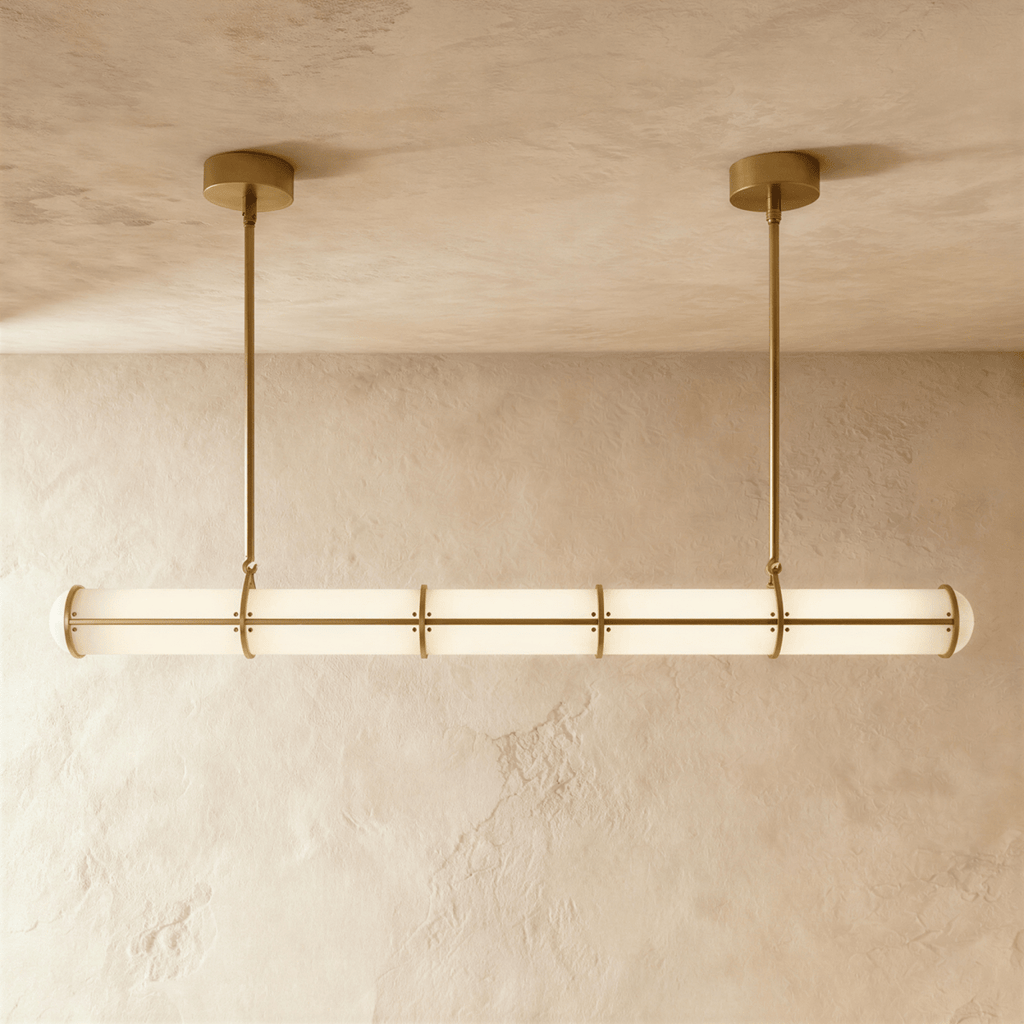 Clérachic long opal tube pendant with brass-gold bands and two slim rods, lit softly against a textured limewash wall.