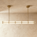 Clérachic long opal tube pendant with brass-gold bands and two slim rods, lit softly against a textured limewash wall.
