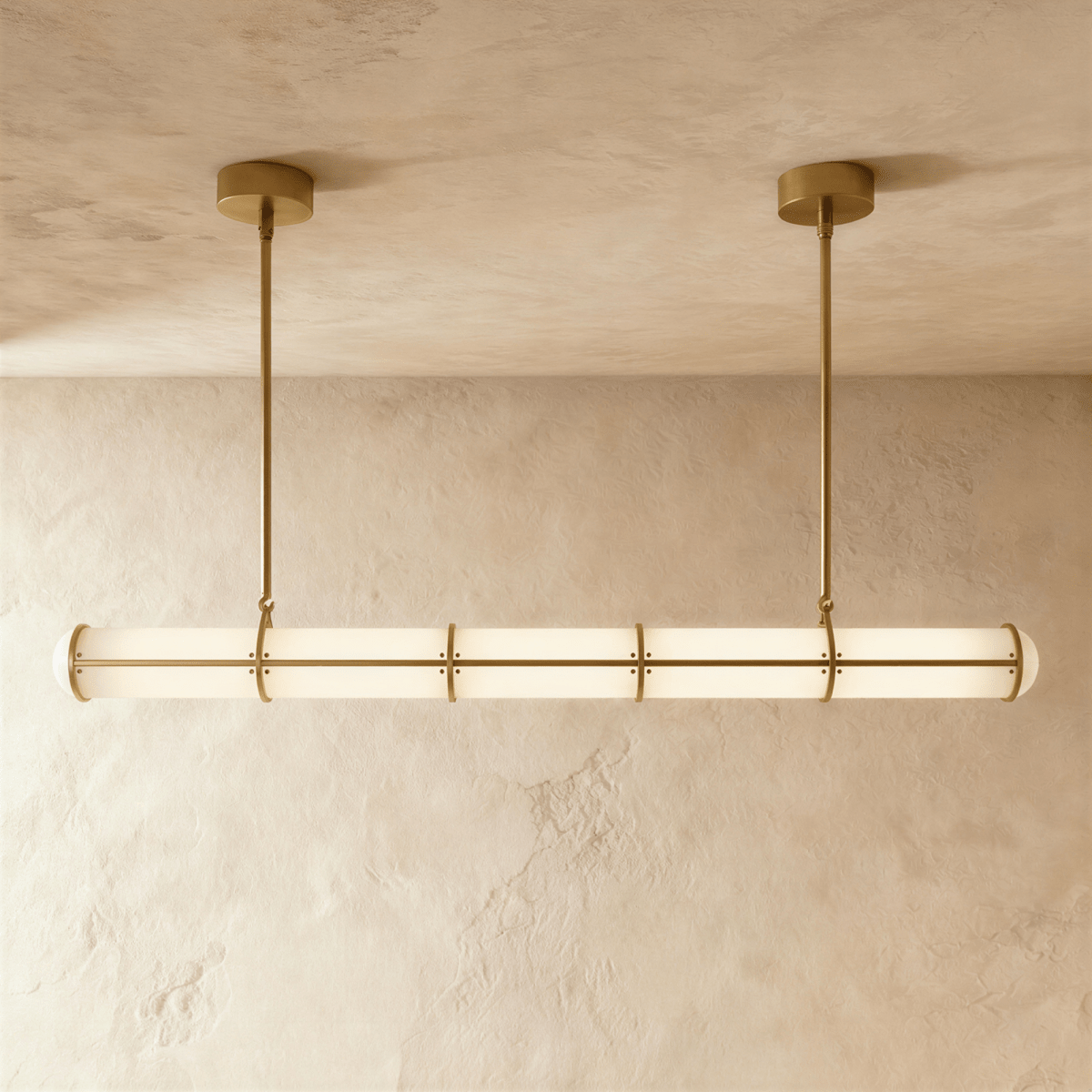 Clérachic long opal tube pendant with brass-gold bands and two slim rods, lit softly against a textured limewash wall.