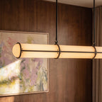 Clérachic black-banded opal tube pendant close up, hung on slim rods with hooks in front of a walnut panel and a pastel painting.