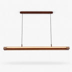 A Clérachic linear pendant with a walnut-toned canopy and a long lit bar hanging on two thin cables, on a plain white backdrop.