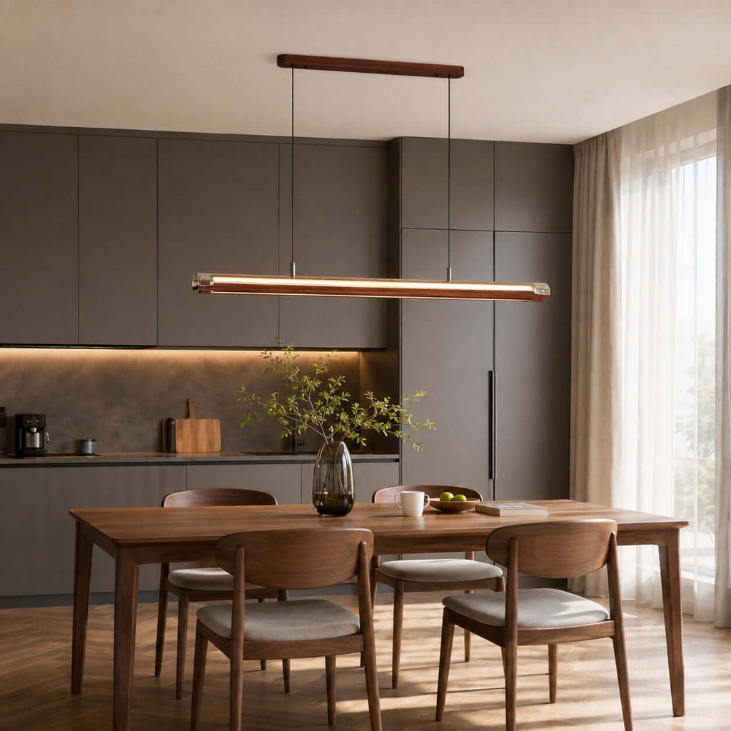 Over a walnut dining table with grey-cushioned chairs, a Clérachic linear pendant glows in front of grey kitchen cabinets.