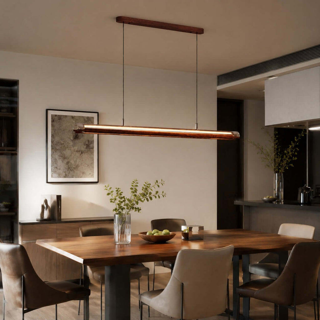 A Clérachic linear pendant hangs over a dark wood dining table in an open-plan room, beside a framed abstract print.