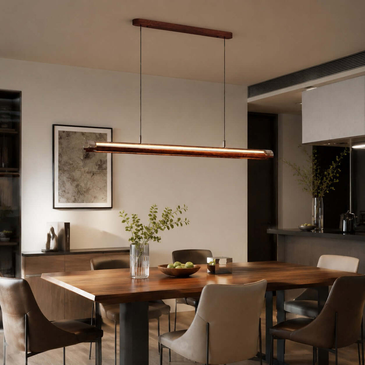 A Clérachic linear pendant hangs over a dark wood dining table in an open-plan room, beside a framed abstract print.