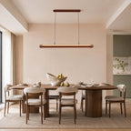 Above a round-based dining table set with bowls and glasses, a Clérachic linear pendant hangs in a soft peach room.