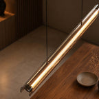 Close view of the glass tube and the warm light strip on this Clérachic linear pendant, with a walnut table below.