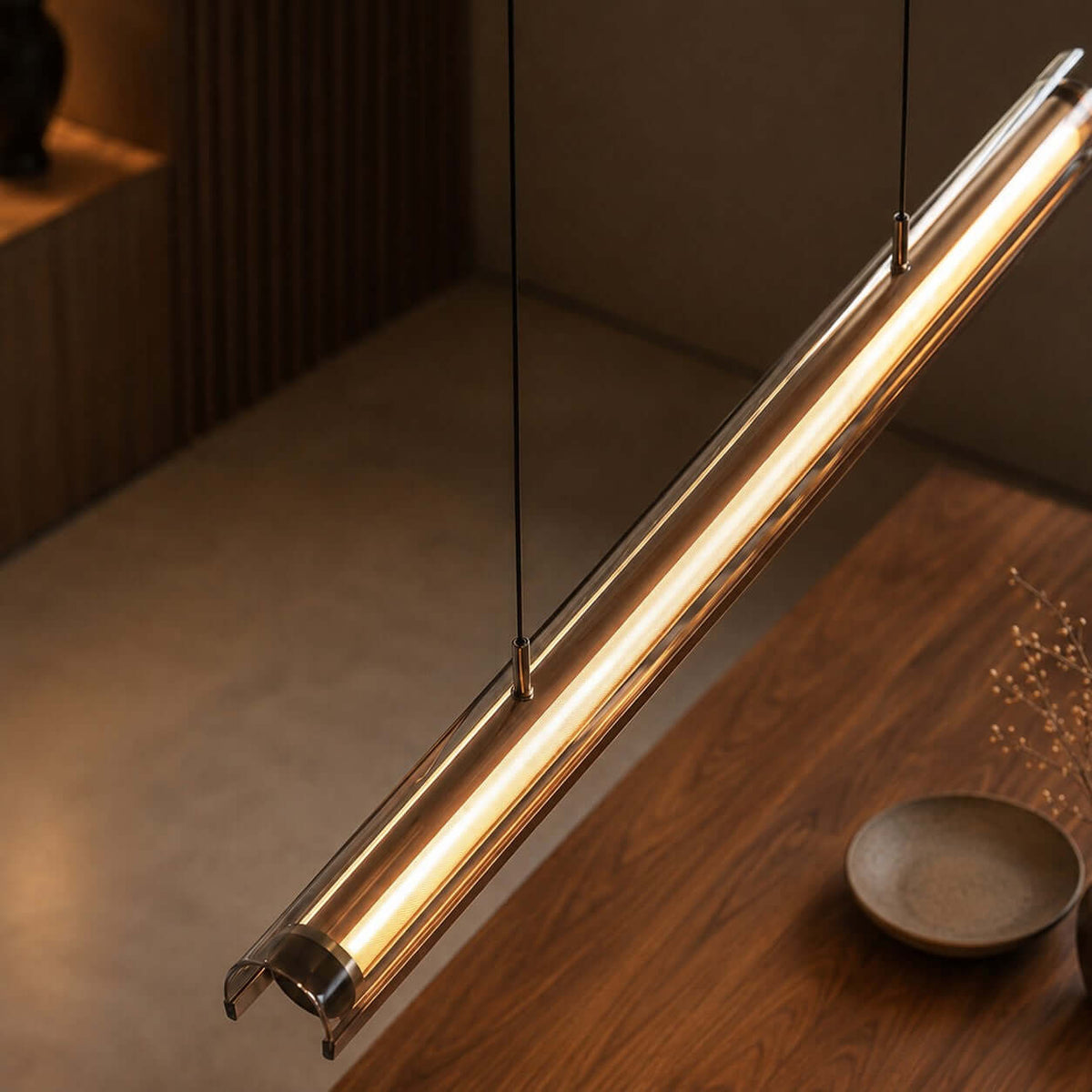 Close view of the glass tube and the warm light strip on this Clérachic linear pendant, with a walnut table below.