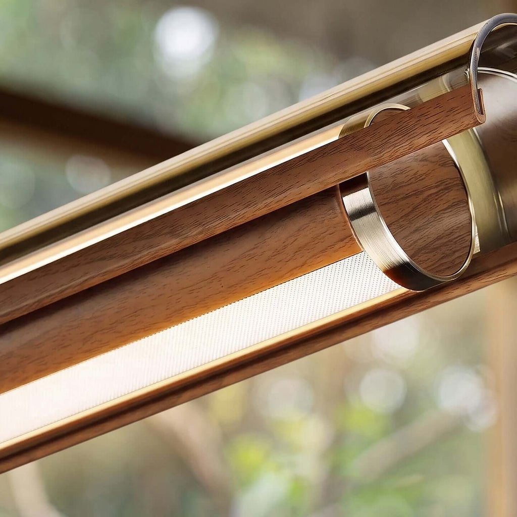 Tight view of the walnut casing, the metal ring and the diffuser strip of this Clérachic linear pendant, with a blurred garden behind.