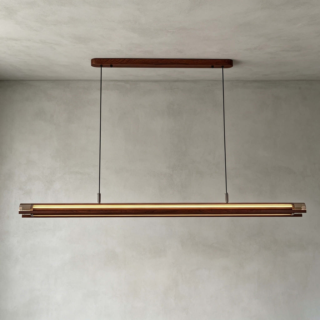 Straight-on view of this Clérachic linear pendant, a lit walnut and gold bar hung from a long walnut canopy, on a grey wall.