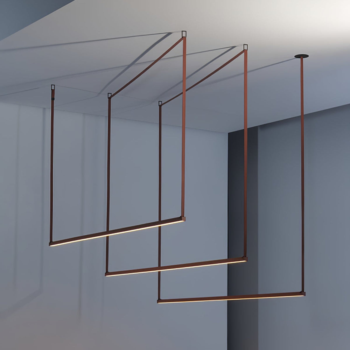 Three red bars of this Clérachic linear pendant light hang in a staggered frame in a blue-grey room, each glowing along its length.