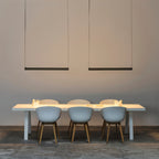 Two black bars of this Clérachic linear pendant light hang above a long white table with pale blue chairs.