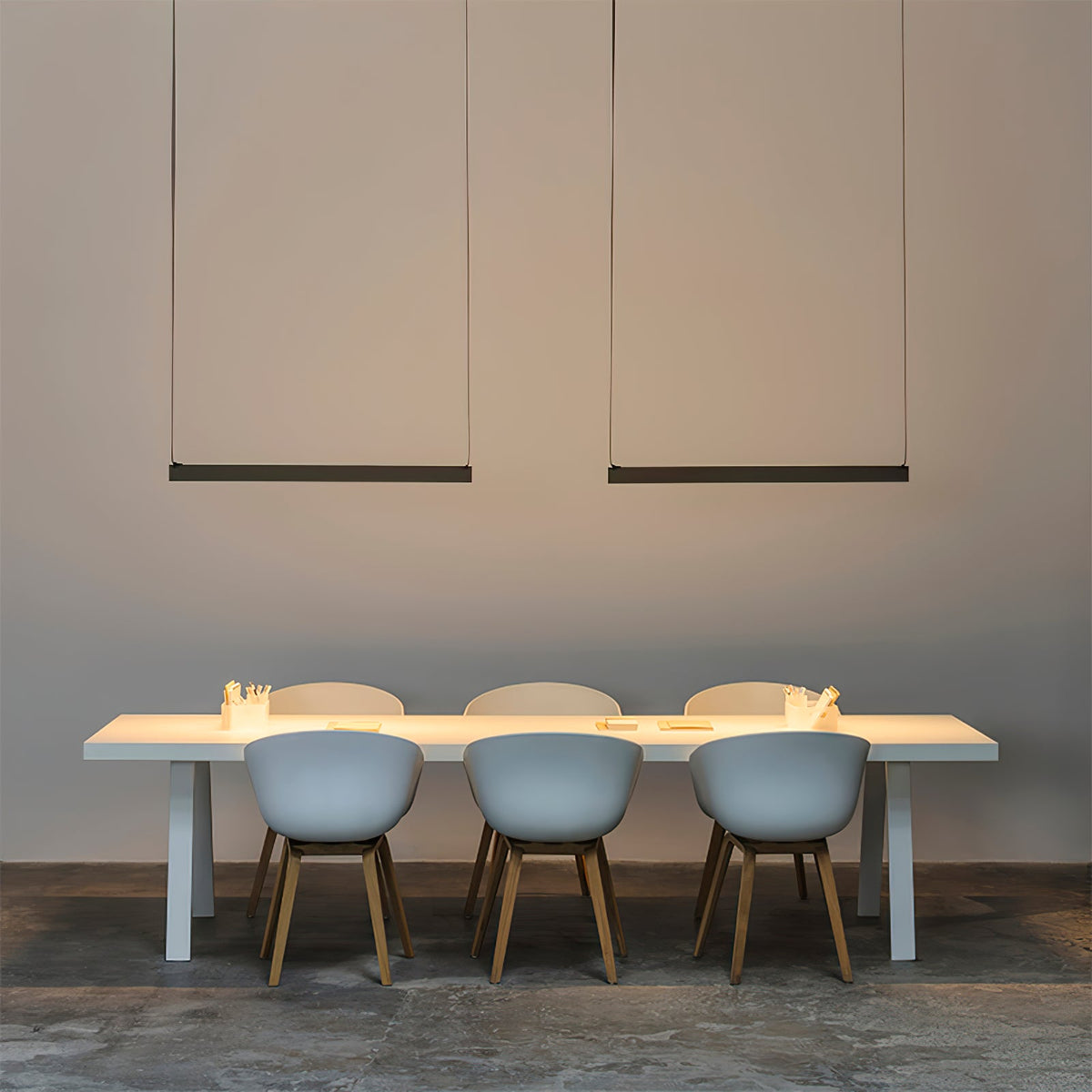 Two black bars of this Clérachic linear pendant light hang above a long white table with pale blue chairs.