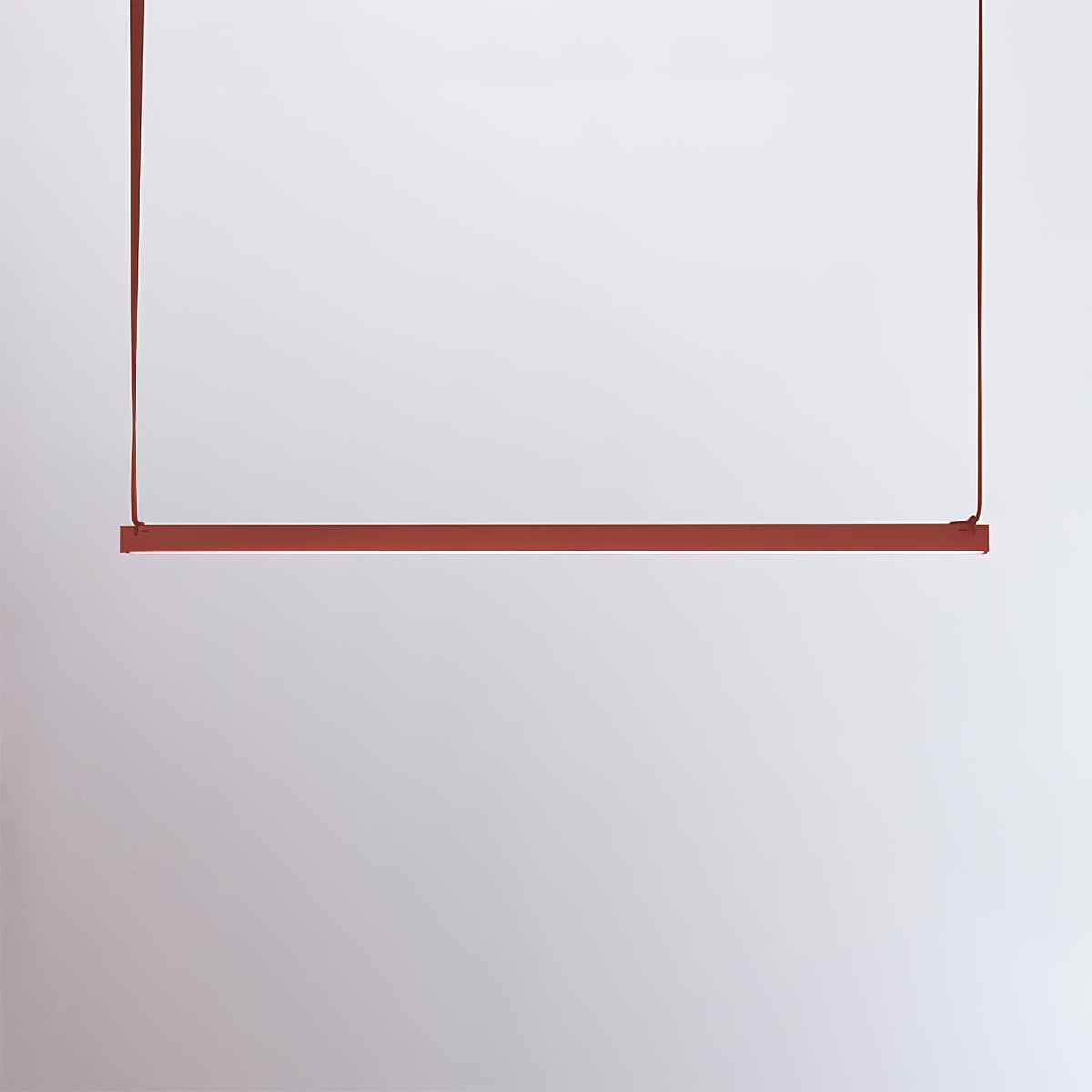 A red bar of this Clérachic linear pendant light hangs from two red straps against a pale lilac-grey wall.