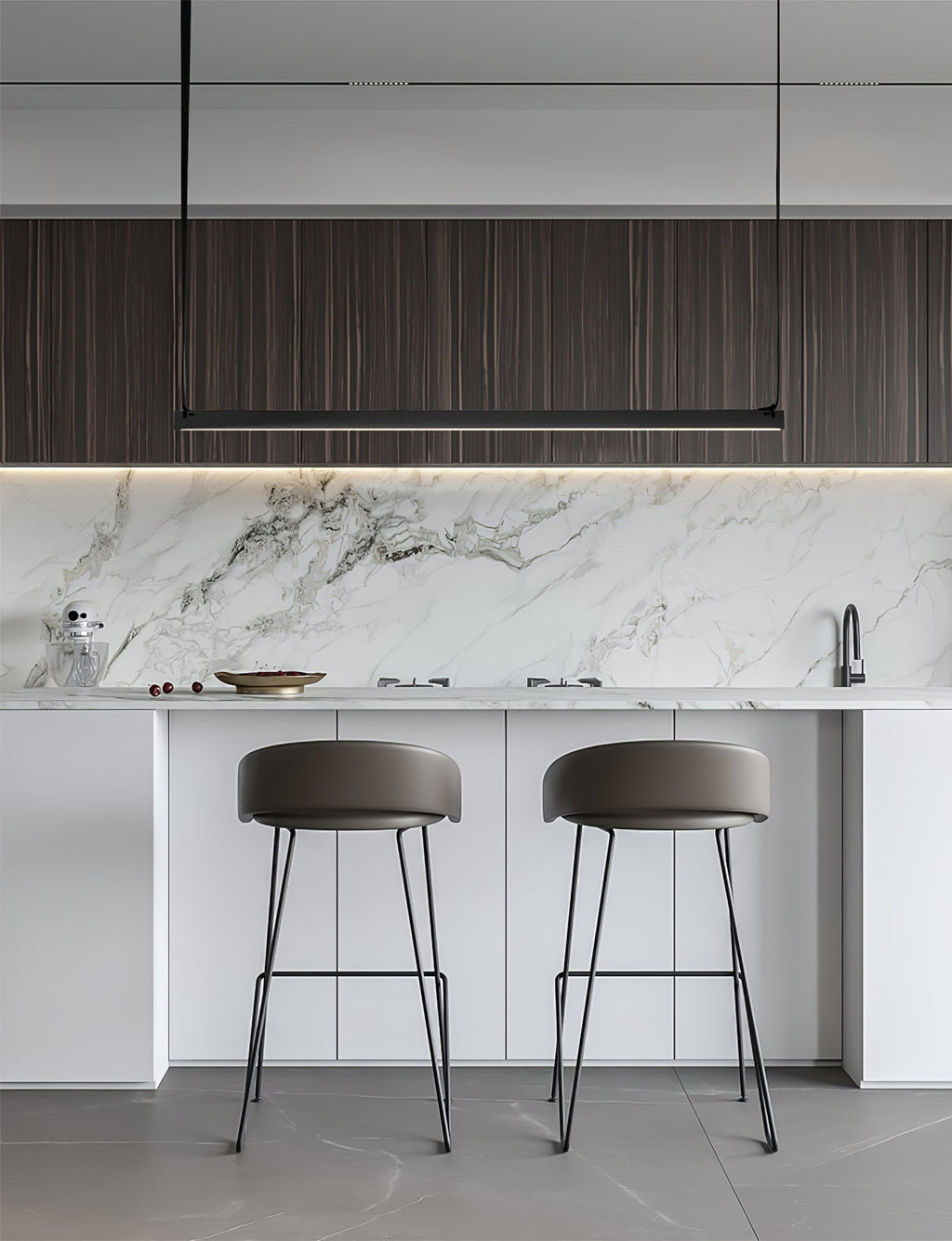 Above a marble splashback and white island with grey stools, this Clérachic linear pendant light hangs as a slim black bar.