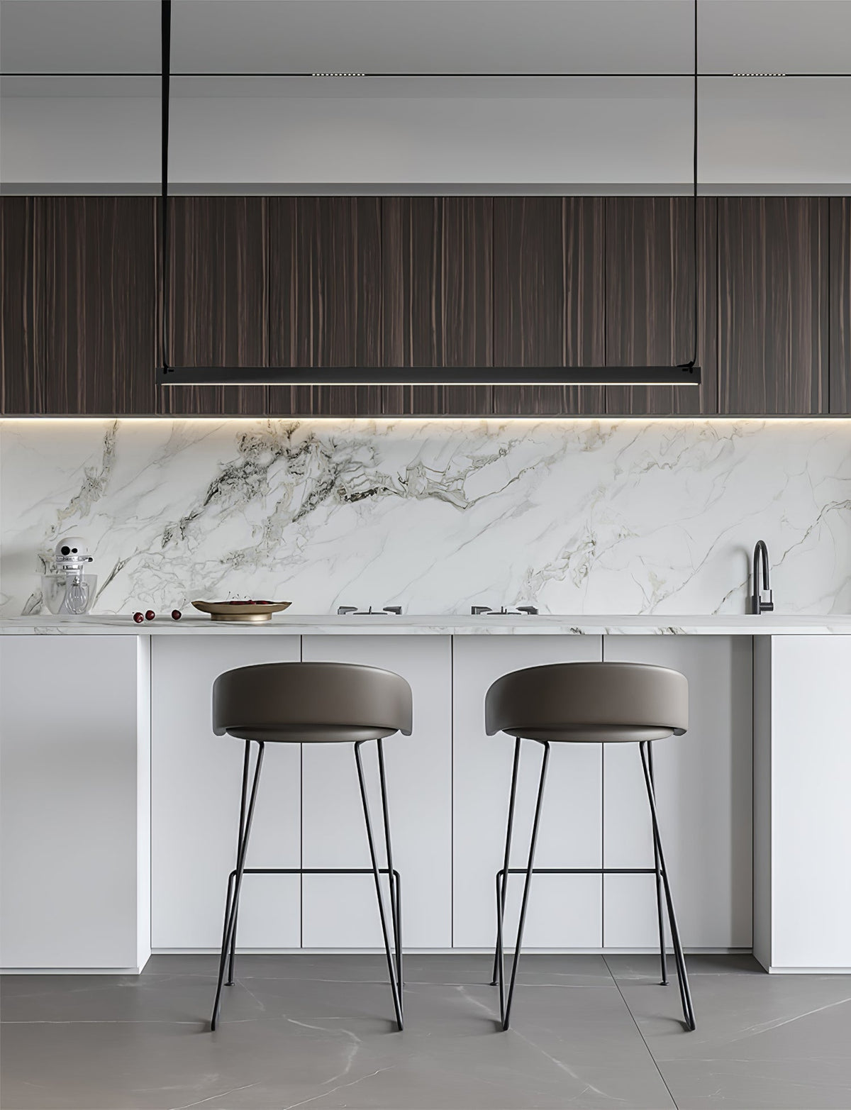 Above a marble splashback and white island with grey stools, this Clérachic linear pendant light hangs as a slim black bar.