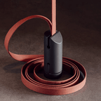 Close view of the red woven strap coiled around a dark metal cylinder, the cable housing of this Clérachic linear pendant light.